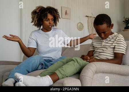 Unzufriedene afroamerikanische Frau Mutter schimpft verärgerten Sohn wegen schlechten Verhaltens zu Hause Stockfoto