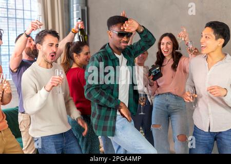Multirassische Freunde tanzen und trinken Wein auf der Geburtstagsparty zu Hause Stockfoto