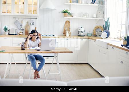 Pretty Girl 12s trägt Kopfhörer und Brille, macht Arbeit, lernt online, hat Sehprobleme, Blinzeln, hat Sehstörungen, Gesundheitsprobleme Stockfoto