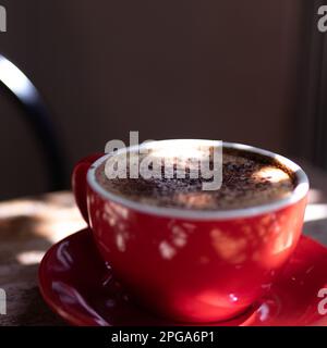 Heiße Schokolade in roter Tasse auf einem Holztisch mit unregelmäßigem Licht Stockfoto