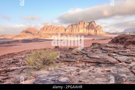 Felsformationen aus rotem Sandstein mit wenigen trockenen Sträuchern oder Büschen im Wadi Rum, auch bekannt als Tal der Mondwüste, Jordanien. Die Morgensonne scheint zu Stockfoto