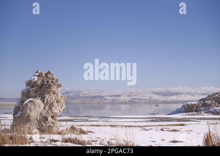 Eine atemberaubende Winterlandschaft mit einem See, umgeben von schneebedeckten Bergen und Felsen Stockfoto