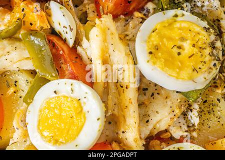 Gomes de sa Kabeljau, in Olivenöl geröstet, mit Tomaten, Paprika, Zwiebeln, gekochten Eiern und Oregano. In einer rechteckigen Backform aus Glas. Stockfoto