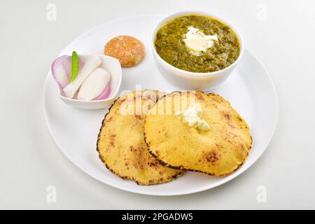 Saag mit Roti serviert mit Jaggery und Salat auf einem Teller isoliert auf weißem Hintergrund Stockfoto