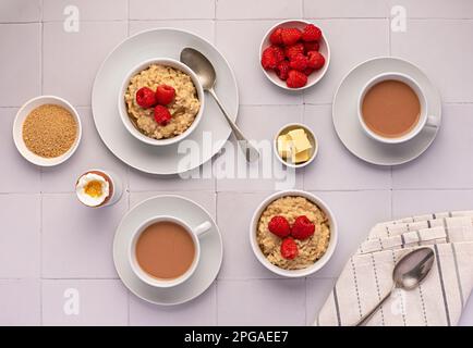 Lebensmittelfotografie von Haferflocken, Hafer, Haferbrei, Frühstück, gekochtem Ei, Tee, Milch, Himbeeren, Butter, Zucker Stockfoto