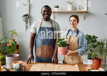 Porträt von zwei lächelnden Gärtnern, die in die Kamera schauen, während sie sich um die Pflanzen im Haus kümmern Stockfoto