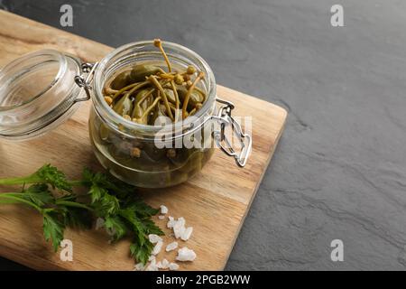 Leckere Kapern in Glasgefäß, Salz und Petersilie auf schwarzem Tisch, Platz für Text Stockfoto