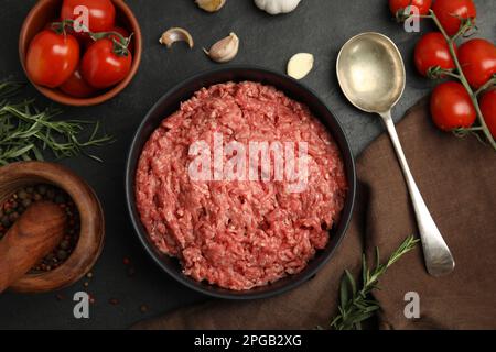 Frisches Hackfleisch in der Schüssel und andere Zutaten auf schwarzem Tisch, flach liegend Stockfoto