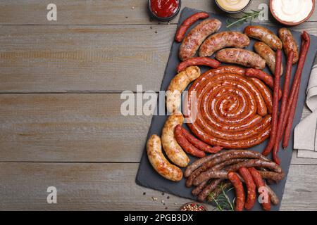 Verschiedene leckere Würstchen und Saucen auf Holztisch, flach liegend mit Platz für Text. Auswahl an Biersnacks Stockfoto