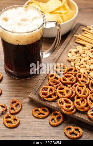 Ein Glas Bier mit leckeren Brezeln-Crackern und anderen Snacks auf einem Holztisch Stockfoto