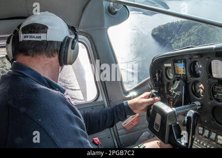 Der Pilot schaut aus dem Fenster eines Wasserflugzeugs, während er nach einem Ort sucht, um das Flugzeug auf dem pazifischen Ozean im Fiordland-Nationalpark, Neuseeland, zu landen. Stockfoto