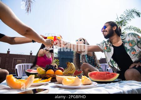 Indische Freunde, die zusammen Spaß haben, Cocktailgetränke anstoßen, Sommerparty feiern, junge Leute mit Gläsern, Toast mit frischem Saft. Schuss aus niedrigem Winkel. S Stockfoto