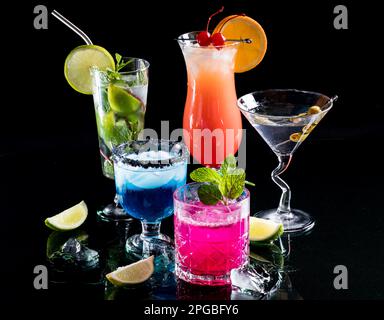 Helle, leuchtende Cocktails, die sich auf Glas vor schwarzem Hintergrund spiegeln. Stockfoto