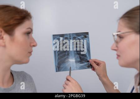 Der Arzt konsultiert eine kaukasische Frau und kommentiert die Röntgenaufnahme der Lunge. Stockfoto
