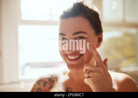 Haut liebt Lotion. Eine attraktive junge Frau, die während ihrer morgendlichen Schönheitsroutine Feuchtigkeitscreme aufträgt. Stockfoto
