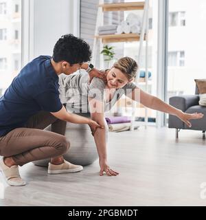 Physiotherapie hilft Menschen jeden Alters. Eine reife Frau, die mit ihrem Physiotherapeuten in einem Rehabilitationszentrum Gleichgewichts- und Bewegungsübungen macht. Stockfoto