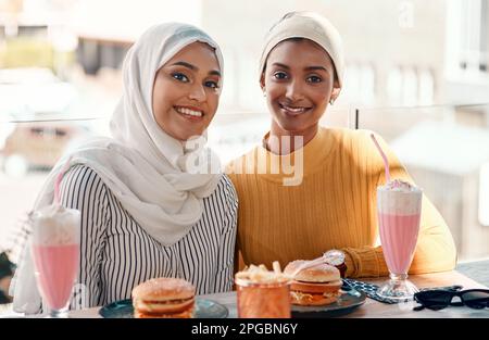 Das ist unsere Art von Wochenende. Gekürztes Porträt von zwei liebevollen jungen Freundinnen, die zusammen in einem Café essen, während sie in Hijab gekleidet sind. Stockfoto