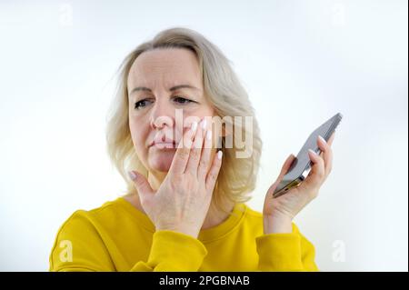 Das Bild eines emotional schockierten jungen Models, das sein Smartphone hält und aufmerksam auf den Bildschirm des Geräts schaut, ihren Mund mit der Hand verdeckt und von Nachrichten überrascht wird. Menschen- und Emotionskonzept Stockfoto