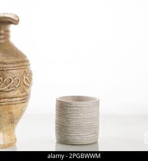 Tonkanne für Wein und ein Tonglas vor dem Hintergrund eines weißen Spiegels. Stockfoto