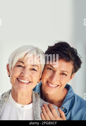 Zwei Generationen dasselbe herrliche Lächeln. Gekürztes Porträt einer liebevollen jungen Frau, die ihre alte Mutter zu Hause umarmt. Stockfoto