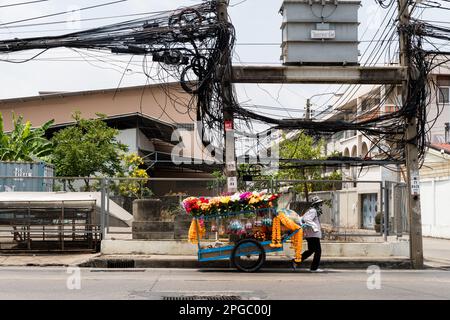 Bangkok, Thailand. 22. März 2023. Ein Blumenverkäufer schiebt seinen Wagen unter elektrische Kabelbündel. Kredit: Matt Hunt/Neato/Alamy Live News Stockfoto