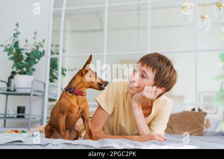 Eine reife Frau liegt auf dem Boden mit einem kleinen Pinscher und genießt den Nachmittag zu Hause, das Konzept des Tieres als Familienmitglied Stockfoto