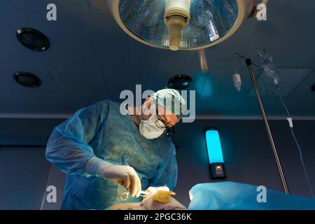 Der Chirurg im Operationssaal steht am Tisch mit dem Patienten unter der Lampe Stockfoto