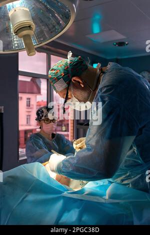Der Chirurg im Operationssaal steht am Tisch mit dem Patienten unter der Lampe Stockfoto