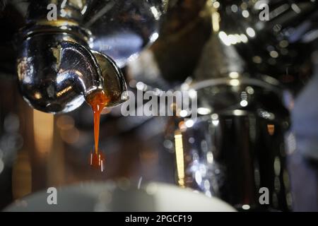 Extreme Nahaufnahme des Beginns des perfekten Espresso-Gießens, wobei der braune Kaffeeschuss vom Griff des einzelnen Portafilters aus Edelstahl tropft. Bari Stockfoto