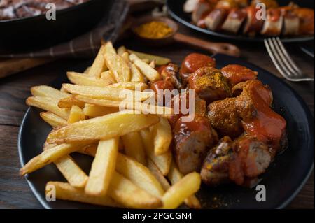 Hausgemachte pommes frites mit deutscher Currywurst auf rustikalem Tisch Stockfoto