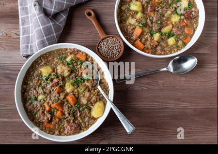 Linseneintopf mit Gemüse, Kartoffeln und geräuchertem Schweinefleisch auf Tellern mit Löffel auf Holztisch von oben Stockfoto