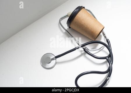 Stethoskop und Kaffee zum Mitnehmen auf weißem Hintergrund. Stockfoto