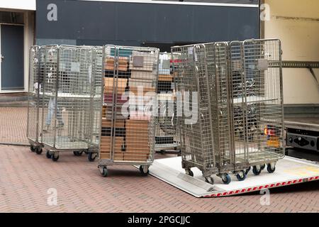 Rollen Sie Container oder Rollkäfigwagen auf der Straße, die von einem Lkw mit offener Klappe entladen werden. Stockfoto