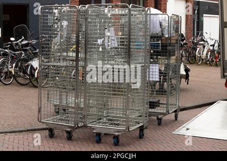 Rollen Sie Container oder Rollkäfigwagen auf der Straße, die von einem Lkw mit offener Klappe entladen werden. Stockfoto