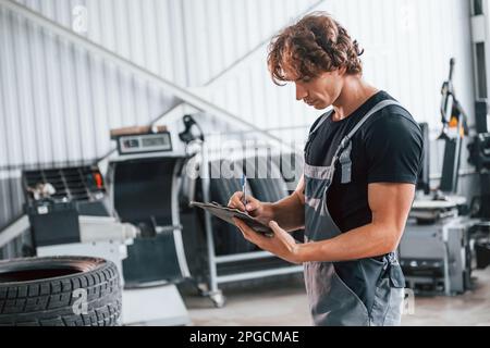 Mit Notizblock in den Händen. Ein erwachsener Mann in grauer Uniform arbeitet im Automobil-Salon Stockfoto