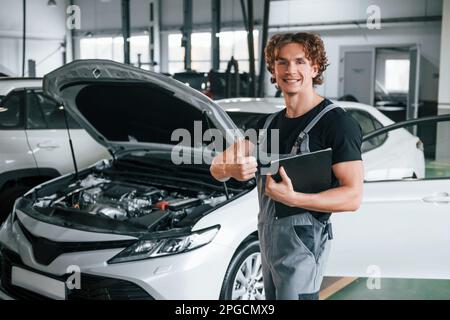 Mit Notizblock in den Händen. Ein erwachsener Mann in grauer Uniform arbeitet im Automobil-Salon Stockfoto