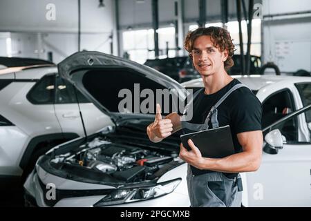 Mit Notizblock in den Händen. Ein erwachsener Mann in grauer Uniform arbeitet im Automobil-Salon Stockfoto