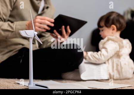 Unerkennbarer bärtiger männlicher Ingenieur in Freizeitkleidung, der auf einem Tablet saß, während er in der Nähe einer Windmühle saß Stockfoto