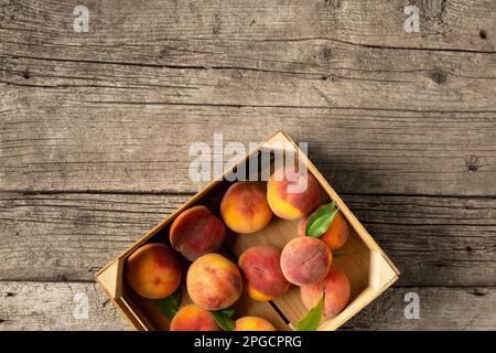 Pfirsiche in einer Schachtel auf einem hölzernen Hintergrund von oben. Frisches Obst auf klassischem Hintergrund. Pfirsiche auf Holzhintergrund. Sommerfrüchte in einer Holzbox. Stockfoto