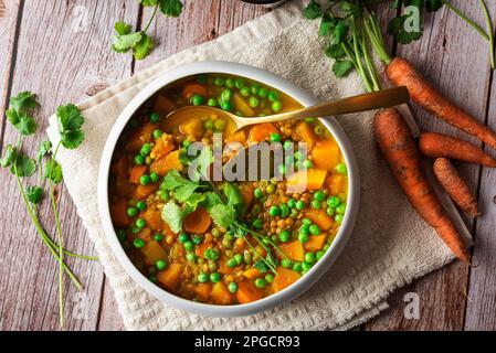 Von oben schmackhafte frisch zubereitete Suppe mit Karotten und grünen Erbsen, serviert in einer weißen Keramikschüssel auf einem Holztisch und dekoriert mit Petersilie-Kleie Stockfoto