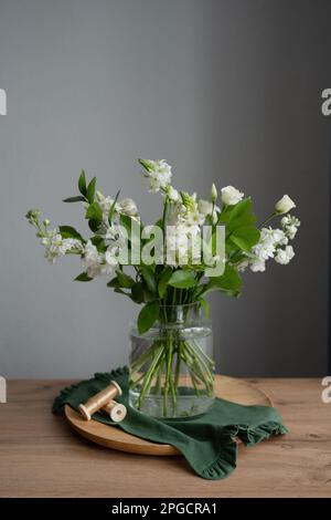 Weiße Blumen in einer Glasvase auf einem runden Holzbrett mit beigefarbenen dekorativen Bändern in einem modernen Blumenladen Stockfoto