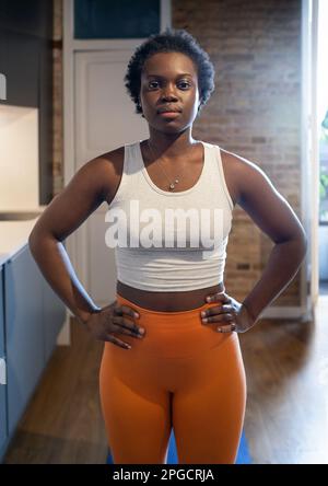 Setze die schwarze Frau in Sportbekleidung ein, stehe im Fitnessstudio mit den Händen auf der Hüfte und schaue in die Kamera Stockfoto
