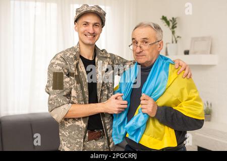 Älterer Vater und Sohn unter ukrainischer Militärflagge Stockfoto