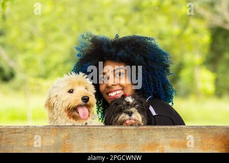 Goiania, Goias, Brasilien – 20. März 2023: Eine junge Frau, die auf einer Parkbank sitzt, lächelt und zusammen mit ihren Hunden zurückblickt. Stockfoto