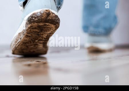 Eine unbekannte Person in blauen Jeans und schmutzigen weißen Schuhen in der Wohnung. Schlammabdruck in Innenräumen auf dem Boden Stockfoto