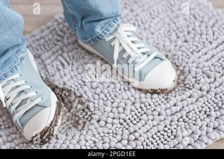 Schlammige Fußabdrücke auf grauem Teppich. Schmutzige Schuhe mit Schlamm und Erde. Täglich schmutziger Fleck Stockfoto