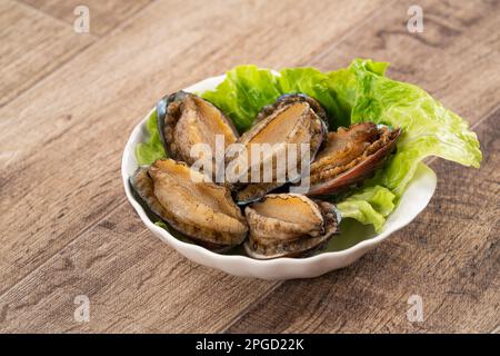 Köstliche rohe Abalone auf einem Teller mit Salat auf Holztisch. Stockfoto