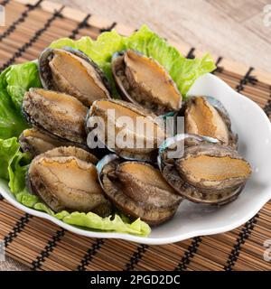 Köstliche rohe Abalone auf einem Teller mit Salat auf Holztisch. Stockfoto