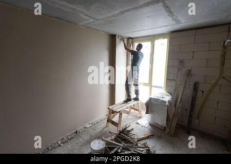 Bauarbeiter tragen Arbeitnehmer insgesamt mit Wand verputzen Werkzeuge Sanierung Appartementhaus. Gipser Sanierung Innenwände und decken mit Stockfoto