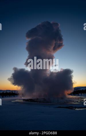 Islands großer Geysir Strokkur im vollen Ausbruch mit Nebel und Rauch, Hintergrundbeleuchtung und dem letzten Licht des orangefarbenen Sonnenuntergangs oder der nahe Dämmerung dahinter Stockfoto